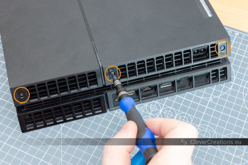 A screwdriver being used to remove a screw at the rear of a Playstation 4.