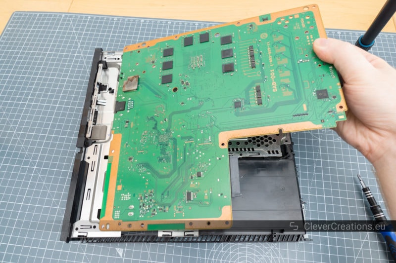 The main circuit board of a Playstation 4 being lifted out of the plastic housing.
