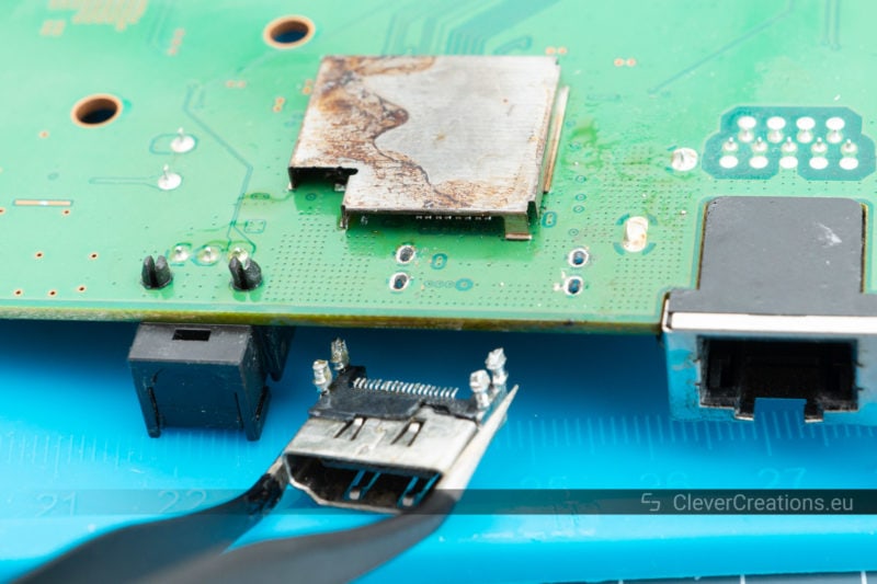 A pair of tweezers being used to remove a desoldered HDMI port from a circuit board.