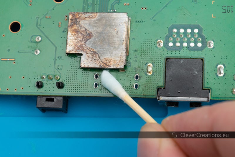 A hand using a cotton swab to clean flux residue from a PCB.