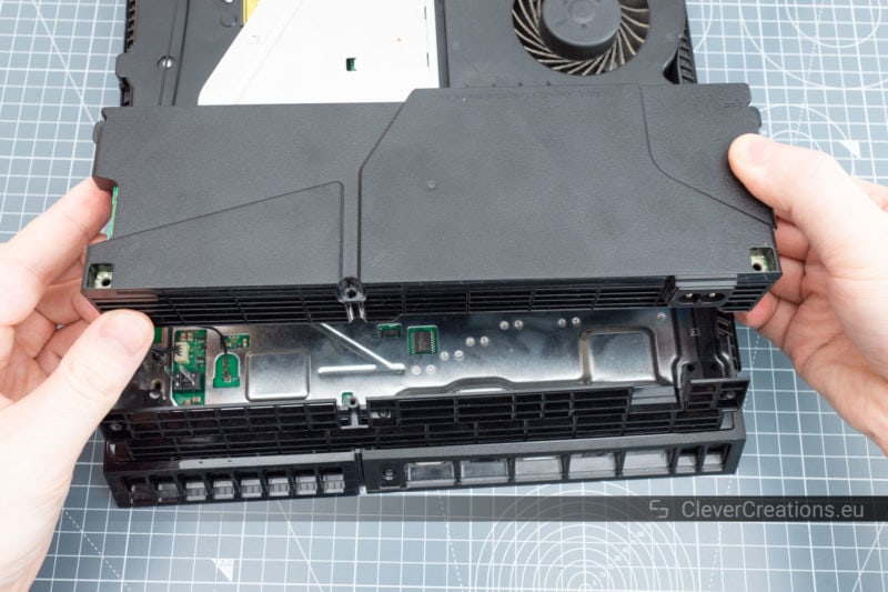 The power supply of a PS4 being lifted out of the console for repair.