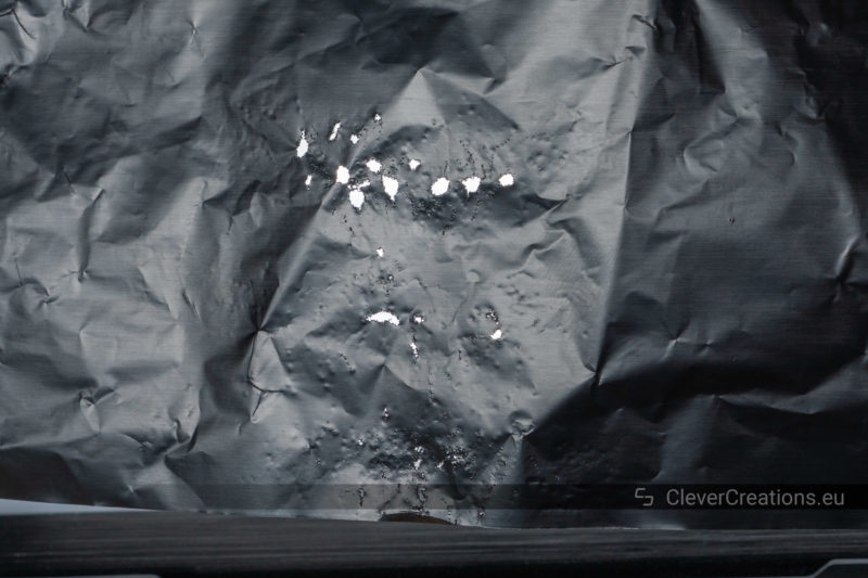 Many perforated holes in a piece of aluminum foil that is being held up against the light after doing the 'foil test'.