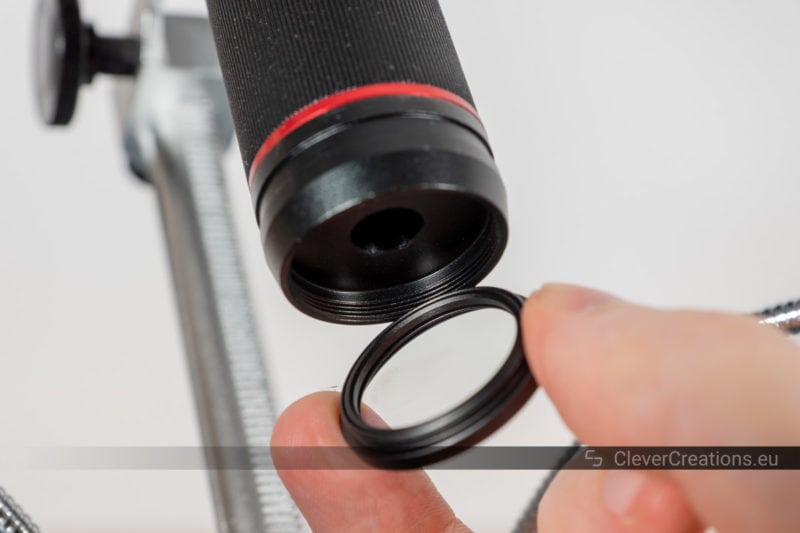 An unscrewed 30mm UV filter held next to an objective lens.