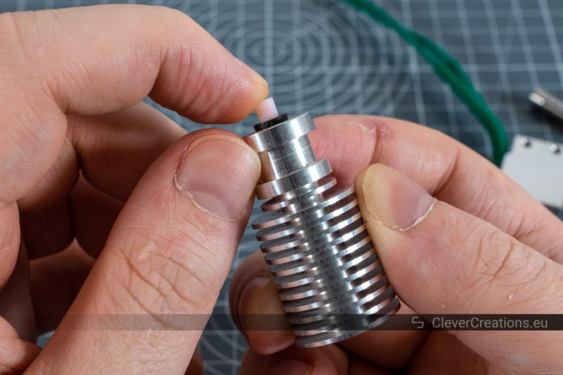 A hand pushing a PTFE tube with stuck filament through the heatsink of a disassembled hotend.
