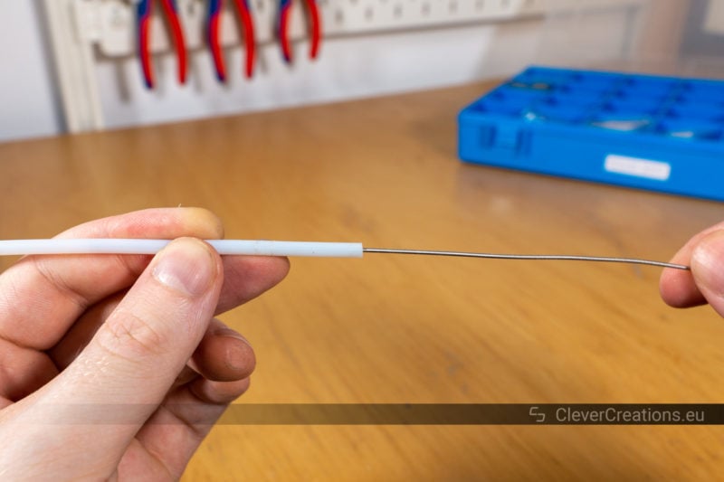 A guitar string being used to remove stuck filament from a PTFE tube.