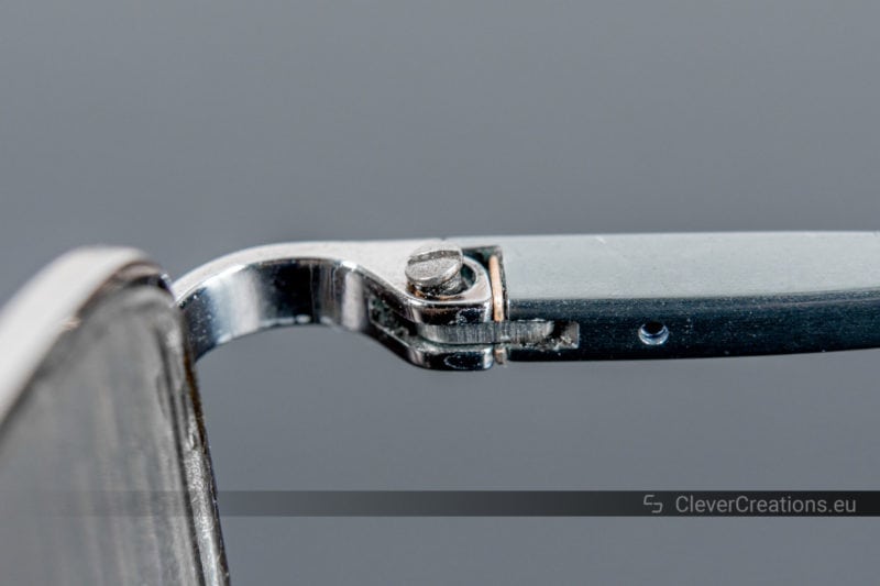 A misaligned screw stuck in the spring hinge of a pair of Ray-Ban eyeglasses.