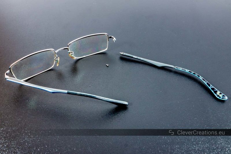 A pair of broken Ray-Ban glasses with a detached loose temple arm.