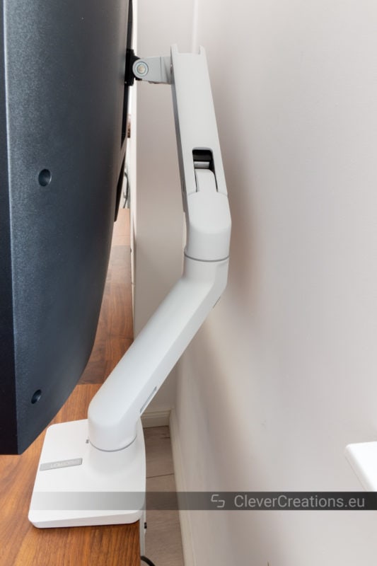 A monitor arm for large monitors positioned partially behind the surface of a walnut desk.