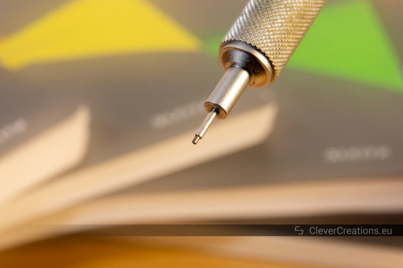 Close-up of a non-retractable lead sleeve on a mechanical pencil in front of a variety of colored notebooks.