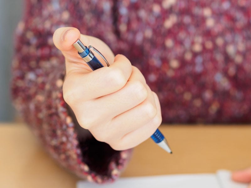 A person using their hand to click the button on top of a pencil.