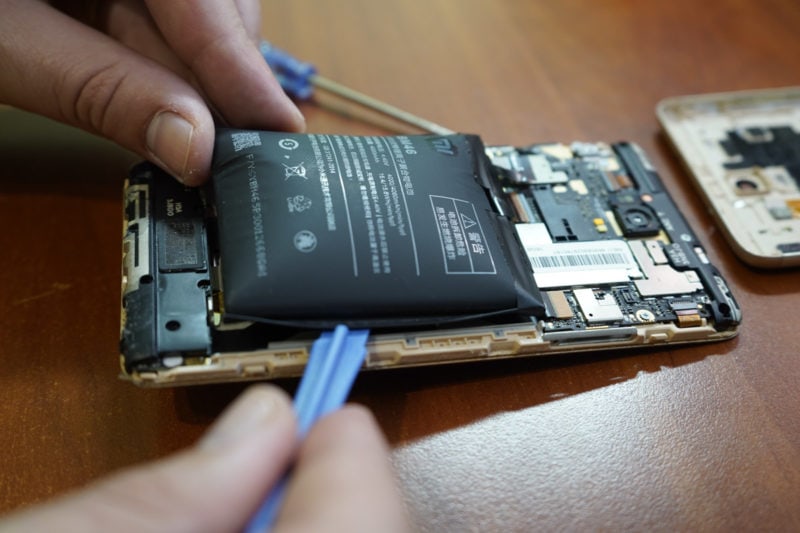 Someone using a plastic spudger to remove a swollen battery from a phone.
