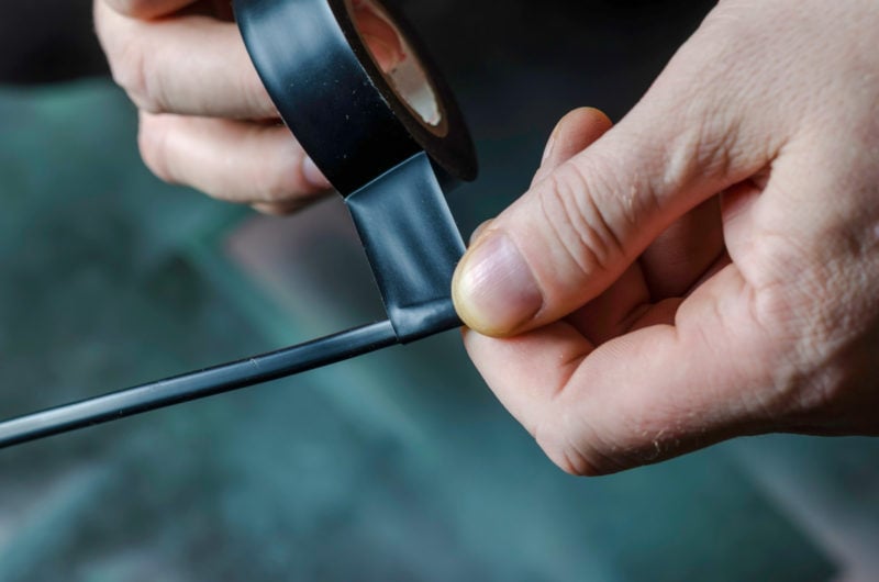 Black electrical tape being wrapped around a single strand of black wire.