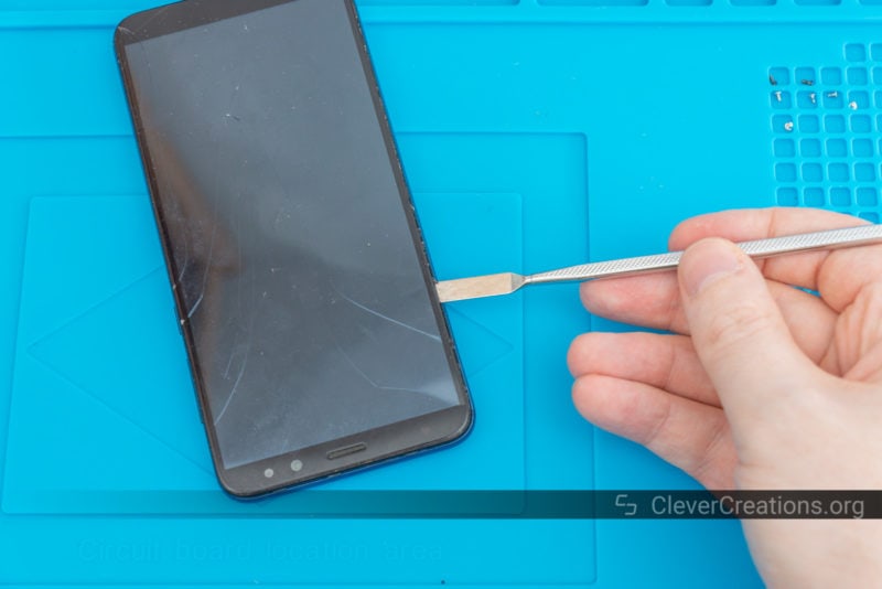 A metal spudger lifting a broken Mate 10 Lite screen out of the device.