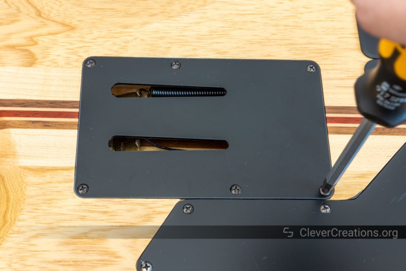A screwdriver removing the screws of a guitar backplate.