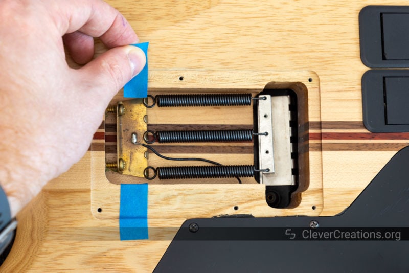 A hand applying pieces of of blue painters tape to indicate the position of a tremolo claw.