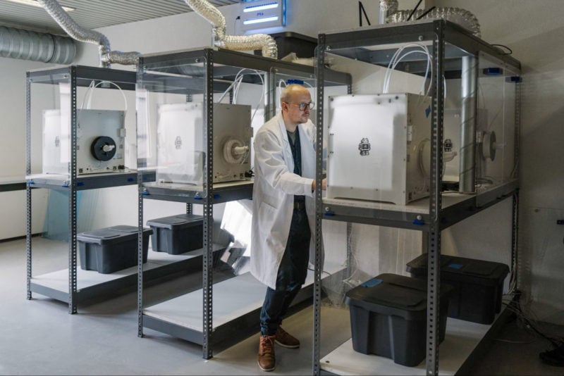 A man standing in between a collection of 3D printers in a print farm