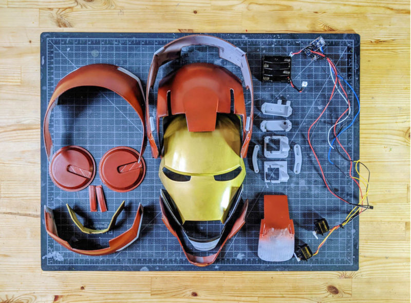 Multiple components (3D printed and electronic) of a Iron Man helmet laid out on a cutting mat.