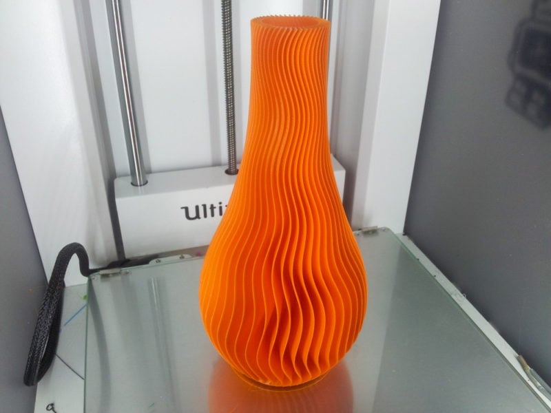A large orange wavy vase on a print bed