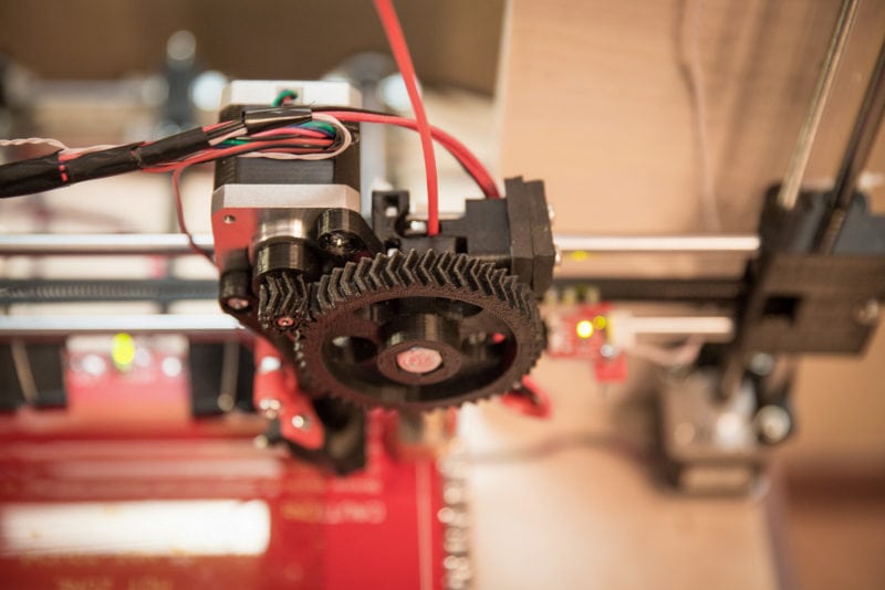 A close-up of a 3D printer extruder with printed gears