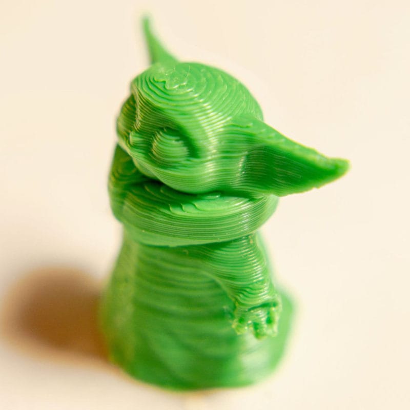 A close-up of a small 3D printed yoda figurine with layer lines