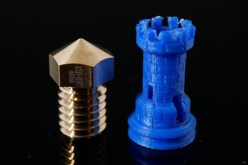 A 0.1mm 3D printer nozzle next to a high-detail print