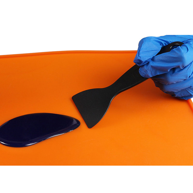 A plastic spatula used to remove spilled resin from a silicone mat