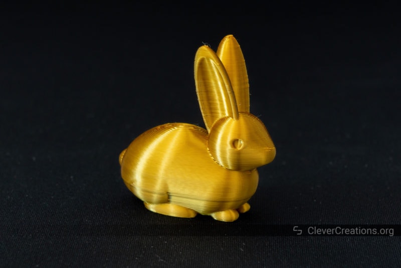 A gold 3D printed rabbit in front of a black background