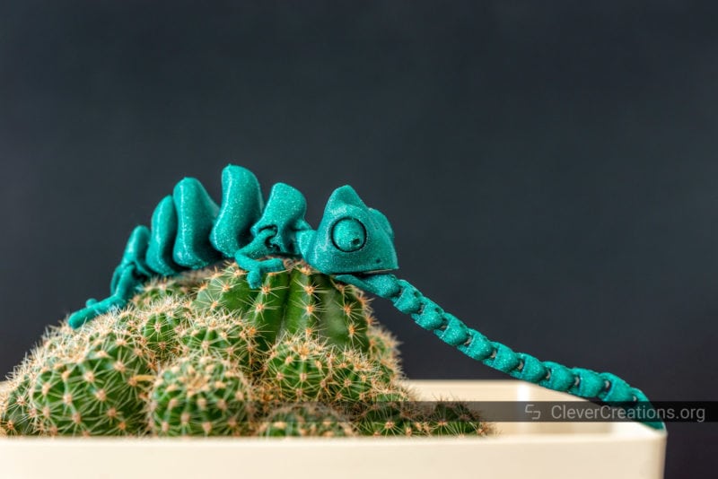 A green 3D printed chameleon placed on top of a cactus on a pot
