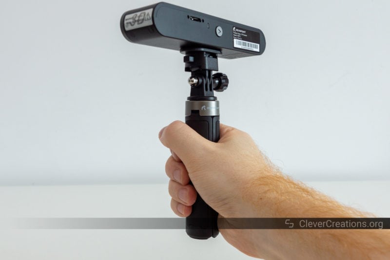 A hand holding a folded in tripod with a Revopoint POP 2 3D scanner mounted on top