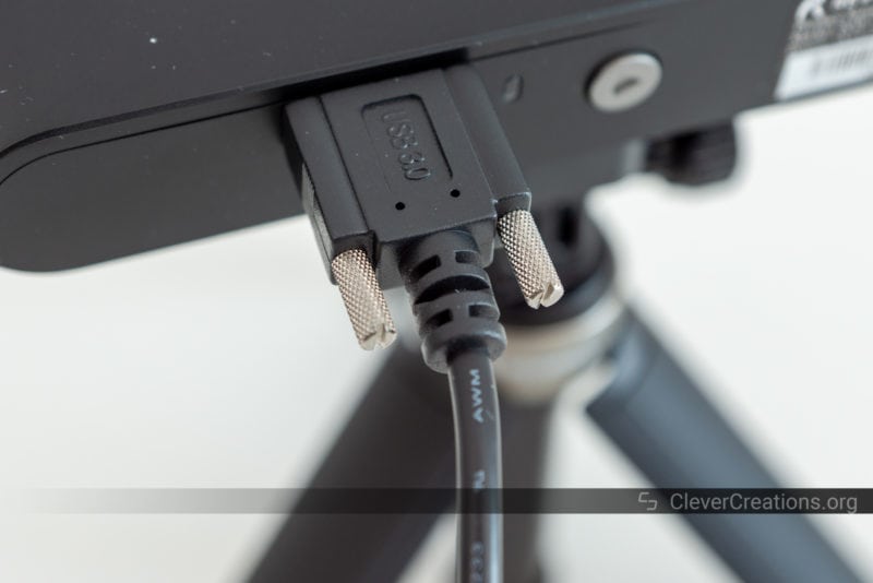 A close-up of a USB 3.0 cable with knurled thumb screws installed in a black electronic device