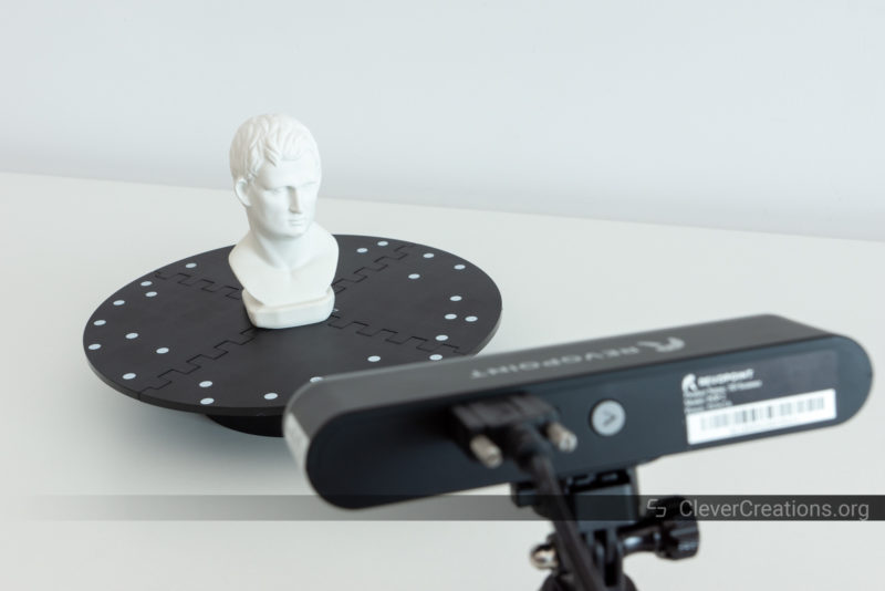 A white statuette on a rotating turntable with tracking marker dots on its surface