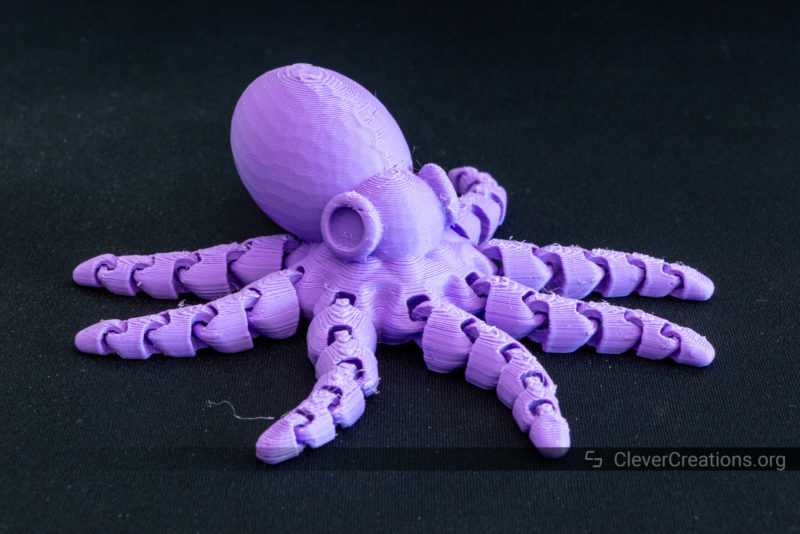 A 3D printed articulating octopus in purple PLA on a black background