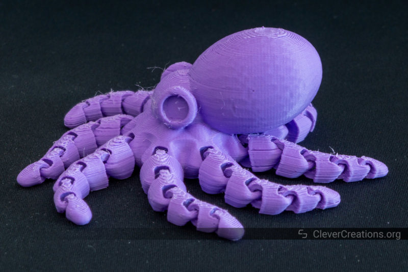 A 3D printed articulating octopus in purple PLA on a black background