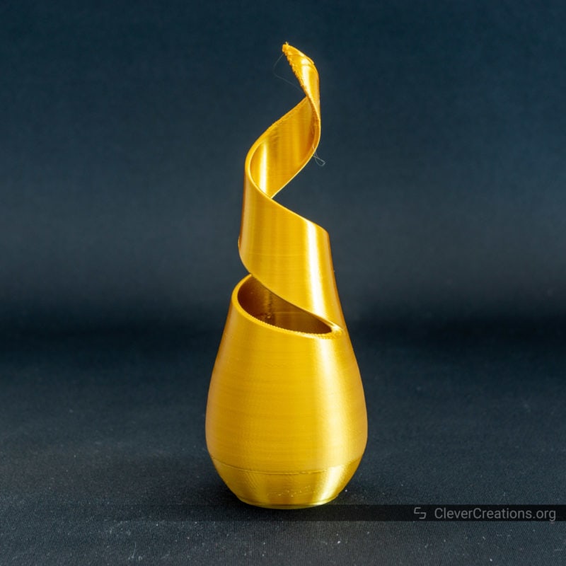 A 3D printed vase in gold high gloss PLA on a black background