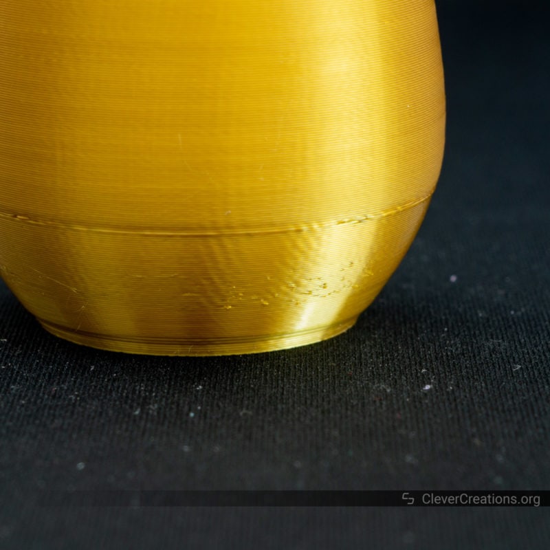 A 3D printed vase in gold high gloss PLA on a black background