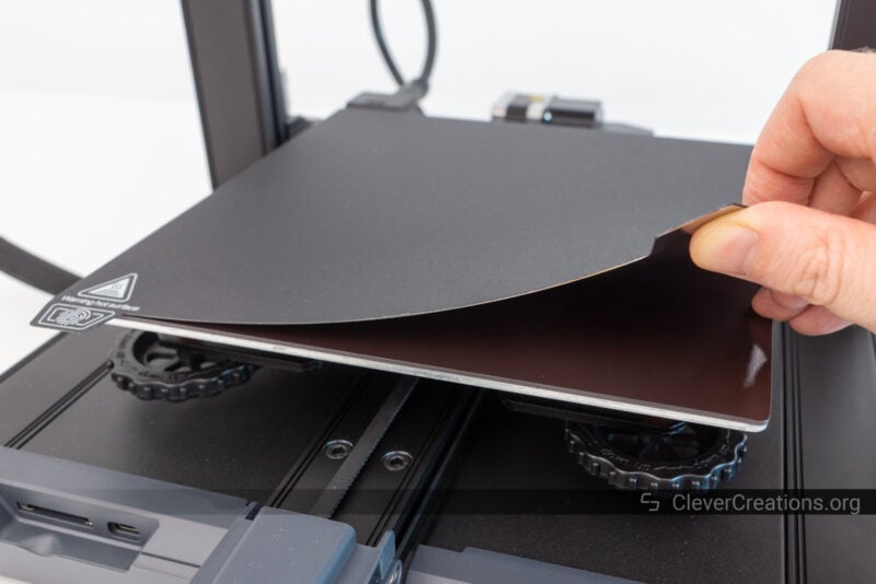 A hand lifting a PC-coated magnetic print surface from a heated bed