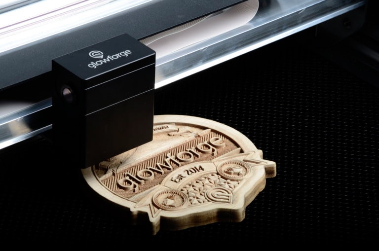 A Glowforge laser cutter with a laser cut wooden logo in it