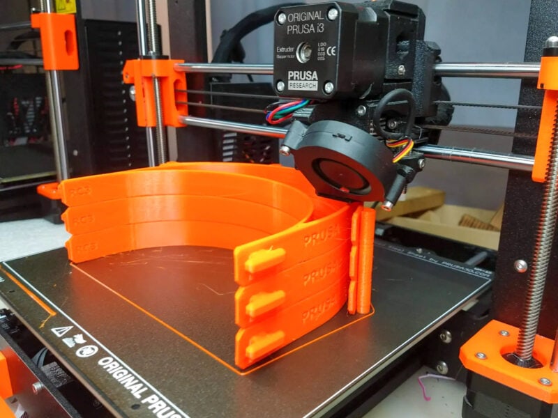 A stack of orange face mask 3D prints in a Prusa MK3 machine
