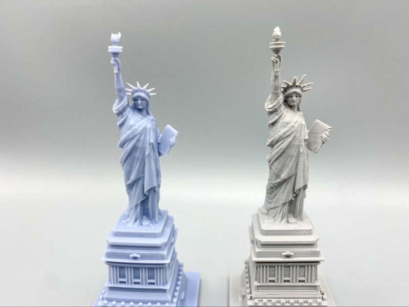 A resin printed vs FDM printed statue of liberty in front of a black background
