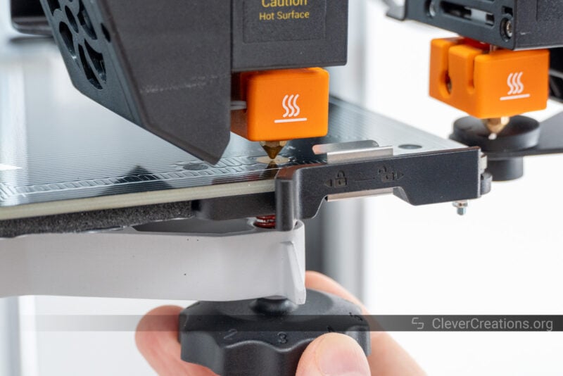 A hand adjusting the leveling knob on the underside of a 3D printer bed
