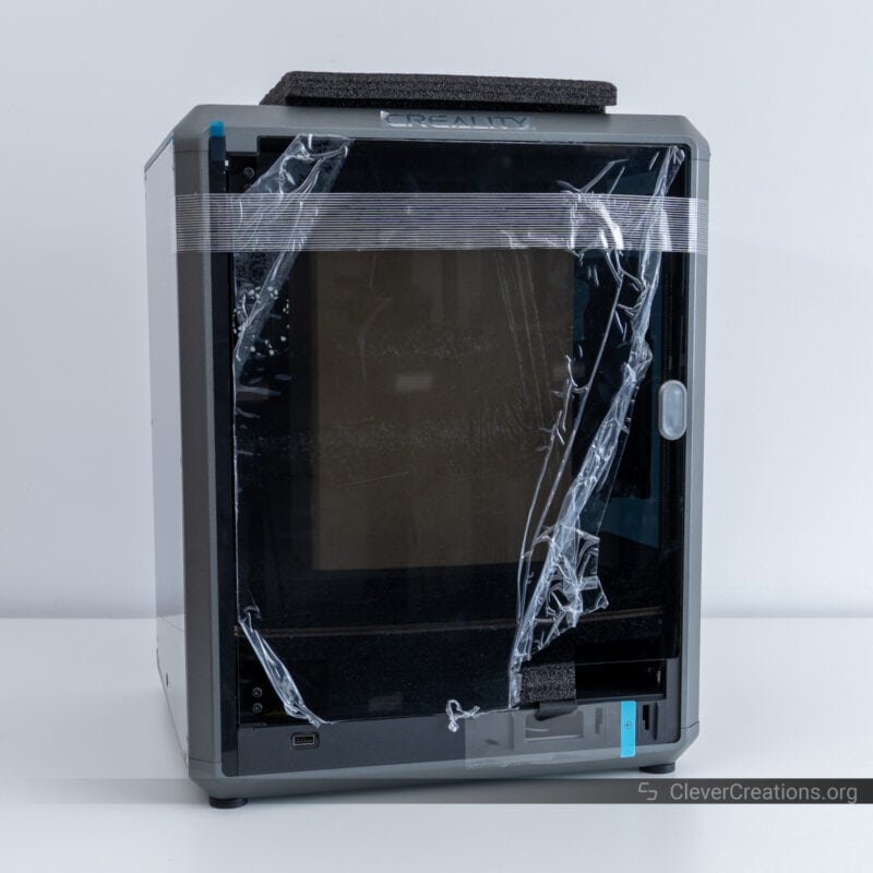 A 3D printer with plastic wrapped around it on a white table in front of a white background