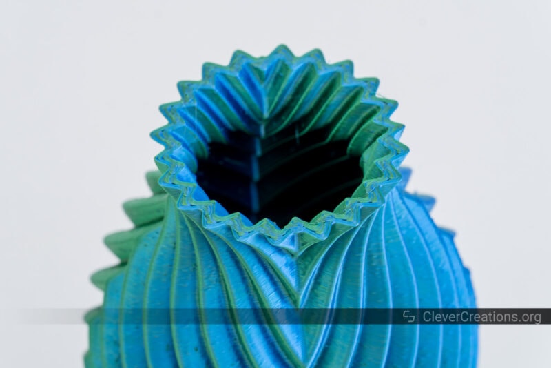 A dual-color blue and green 3D printed vase with visible artifacts on its external shell