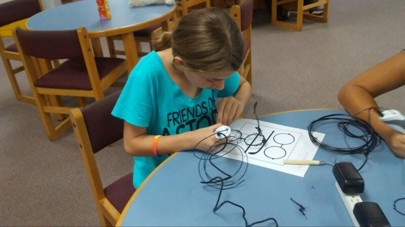 A kid using a 3D pen with black filament material