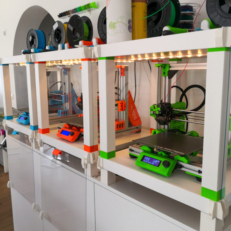 A collection of 3D printers in partial LACK IKEA enclosures.