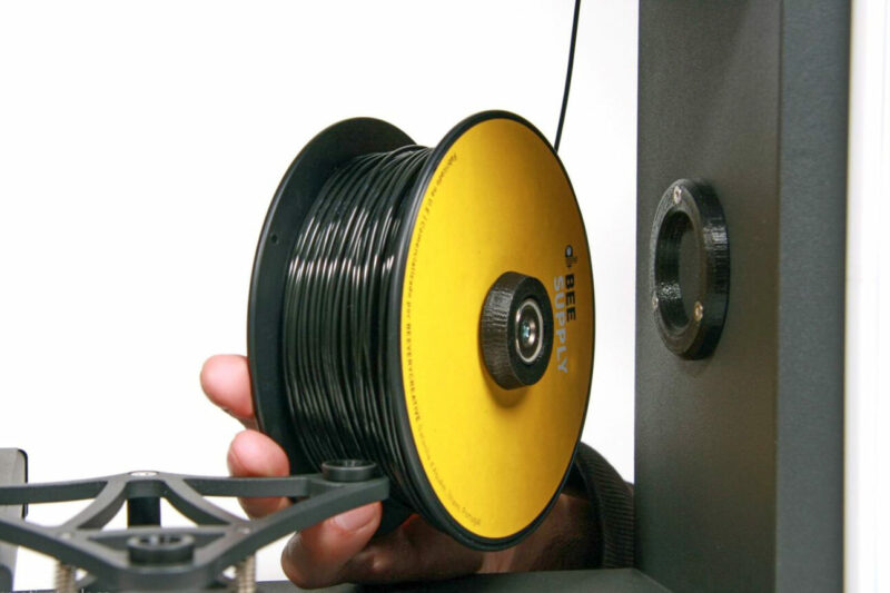 A hand mounting a spool of filament like ABS into a 3D printer.