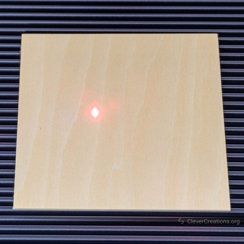 Two red laser dots overlapping on a piece of square wood, indicating that the machine is in focus.
