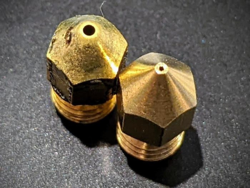 Two 3D printer nozzles, one with a degraded opening and one that is still in good condition.