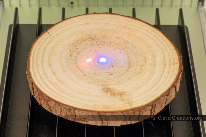 A round wooden coaster with a red and a blue laser dot one centimeter apart.