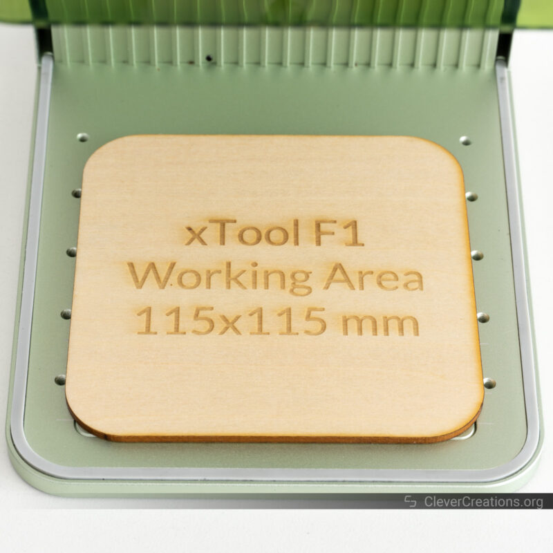 A wooden board with engraved text 'xTool F1 Working Area 115x115 mm'.