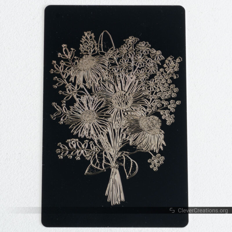 An outline of a bouquet of flowers that has been scored on a metal business card with the xTool F1.